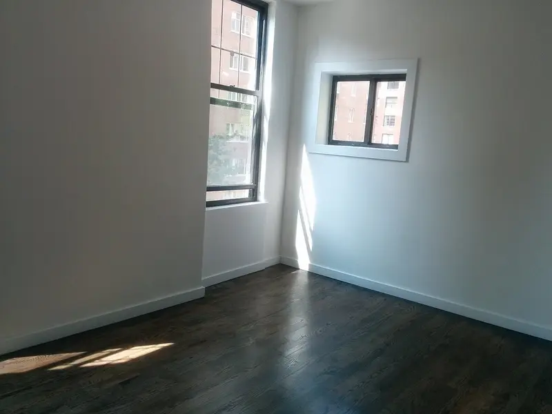Habitación vacía con suelo de madera oscura y ventanas en esquina